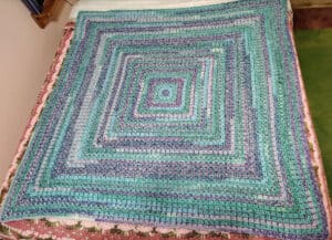 Vibrant turquoise and purple crochet blanket showcasing intricate granny square pattern by The Crochet Crowd.