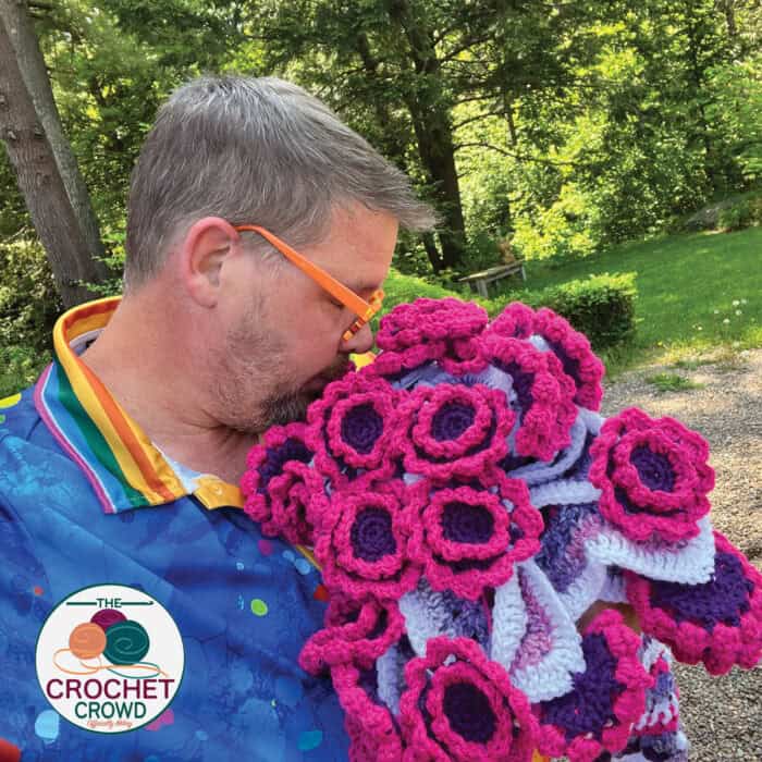 A man wearing glasses holding a crocheted flower.
