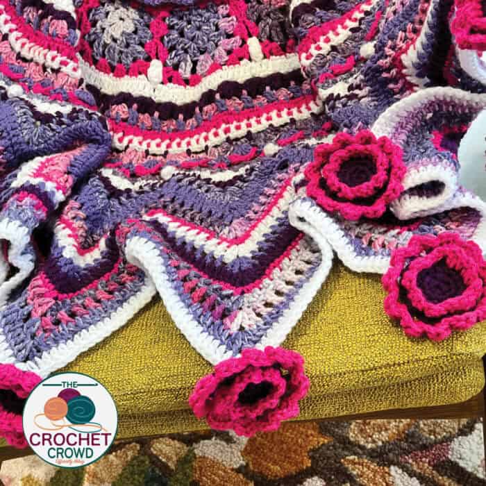 A crocheted blanket with pink and purple flowers.